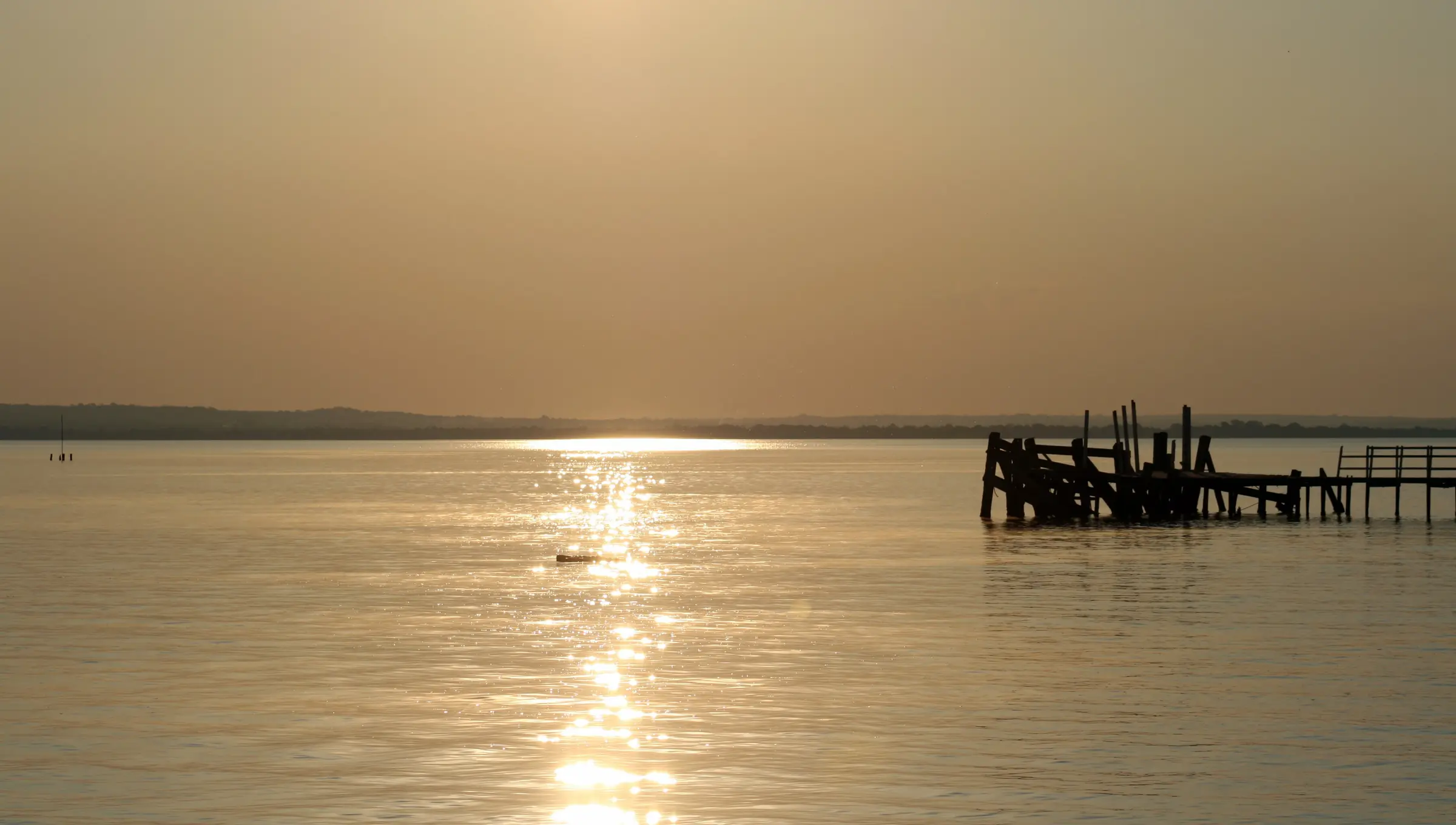 Atardecer sobre el lago Ypacaraí, con un viejo muelle de madera